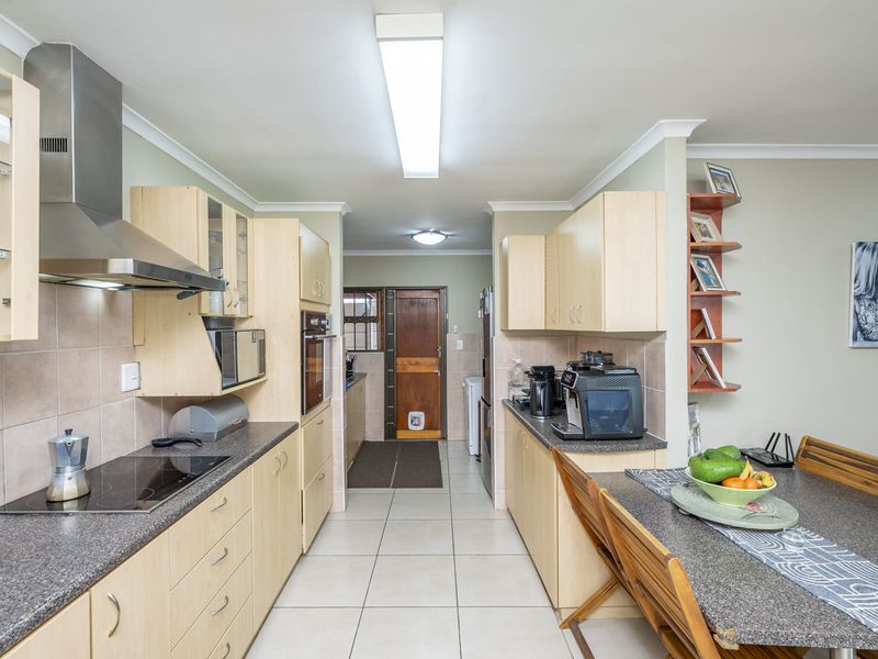 Functional kitchen featuring light wood cabinetry, dark countertops, integrated appliances, and tiled flooring, leading into a secondary utility or scullery area.