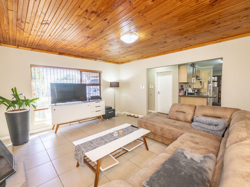 Open plan living area featuring tiled floors and a timber tongue and groove ceiling, flowing into a functional kitchen space with breakfast bar.