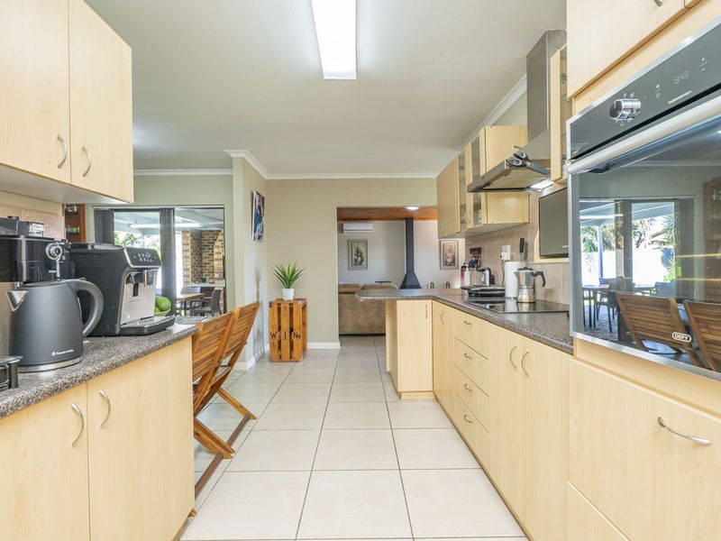 A functional kitchen featuring light wood cabinetry, laminate countertops, built-in oven, and electric hob, with ceramic floor tiles throughout.