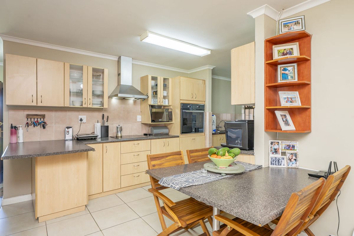 A functional kitchen featuring light wood cabinetry, laminate countertops, built-in oven, stainless steel extractor fan, and tiled flooring with an integrated dining area.