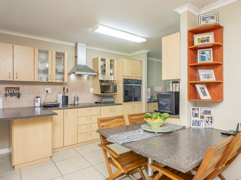 A functional kitchen featuring light wood cabinetry, laminate countertops, built-in oven, stainless steel extractor fan, and tiled flooring with an integrated dining area.