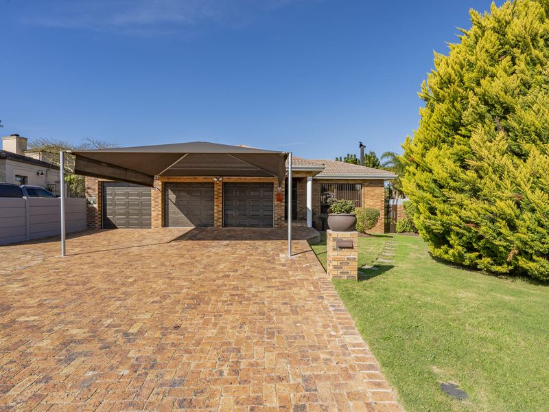Front elevation of a brick house featuring a triple garage, a paved driveway with a shade sail carport, and a well-maintained front garden.