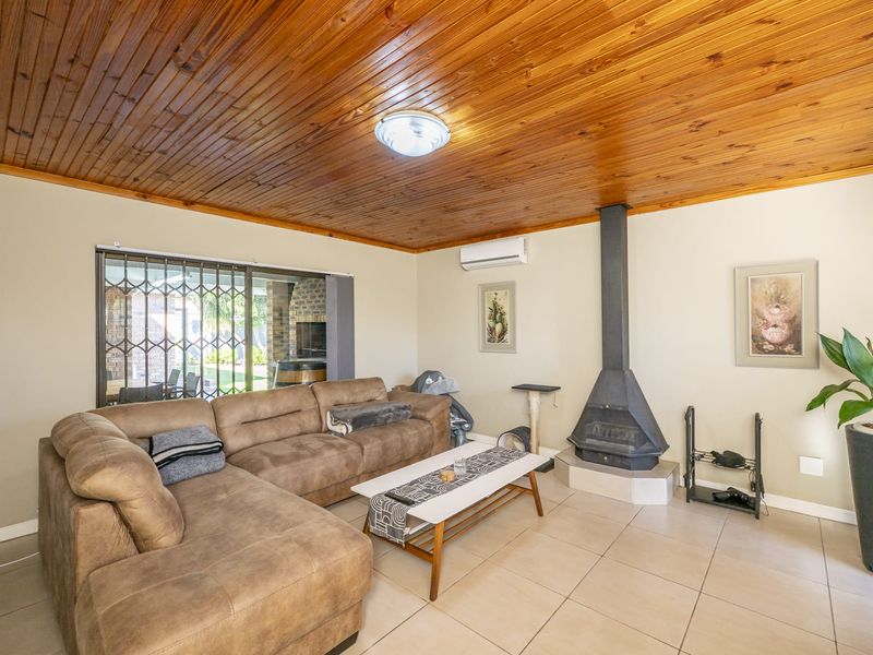 Comfortable living room featuring a wood-paneled ceiling, tiled flooring, a freestanding fireplace, and a split-system air conditioner, with access to an outdoor patio area.