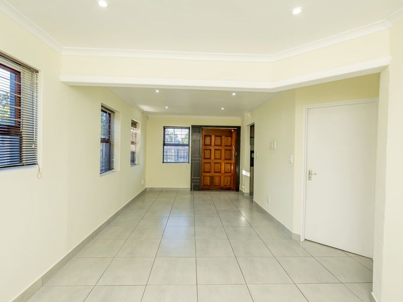 A bright, empty living area featuring neutral tiled floors, recessed downlighting, and a solid timber front door with modern finishes.