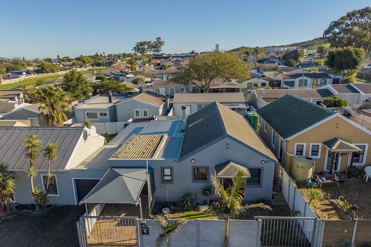 Aerial view of a residential property featuring a grey house with a corrugated metal roof, carport, and secure boundary walling in a suburban neighborhood.