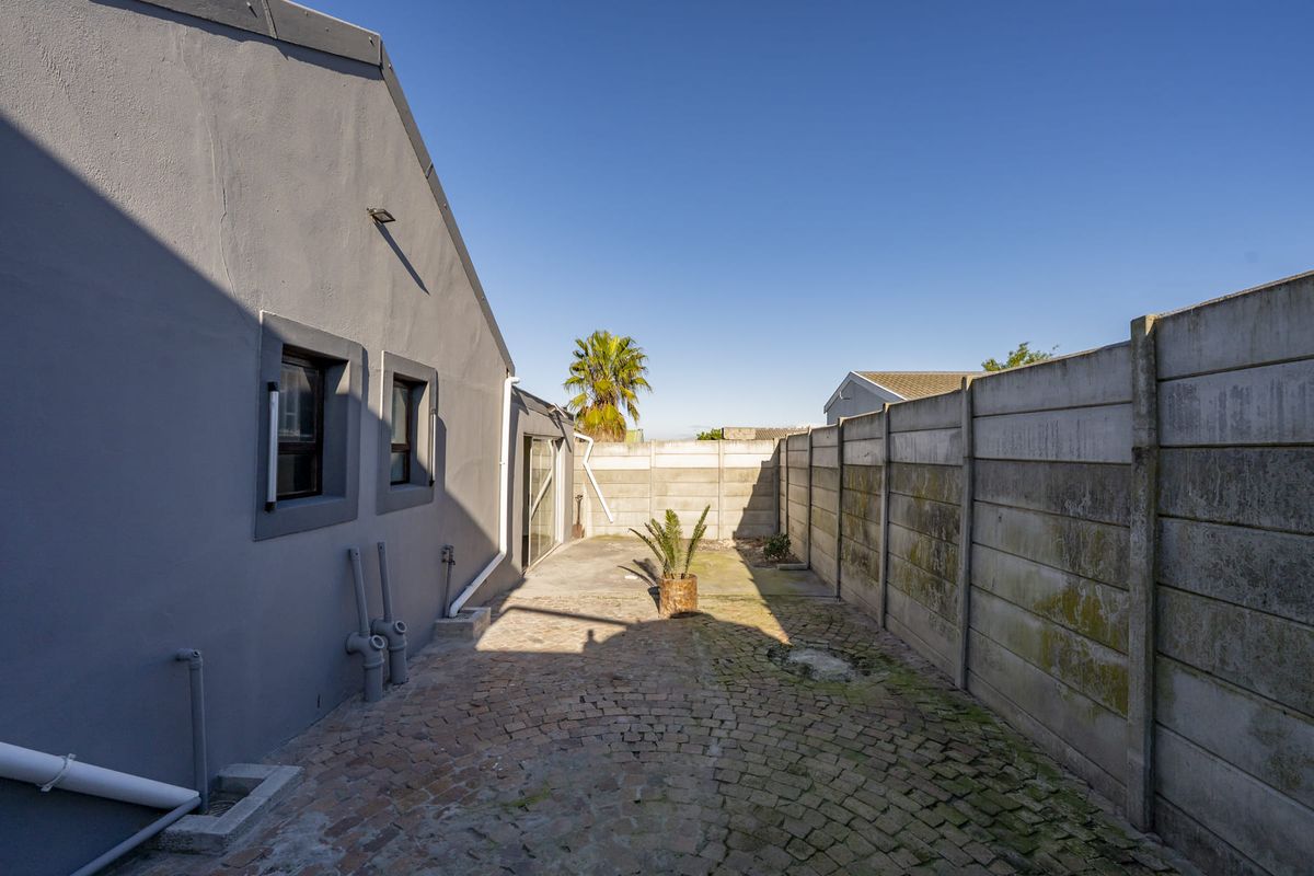 A rear exterior area featuring cobblestone paving, a sliding glass door, and a precast concrete boundary wall with visible weathering.