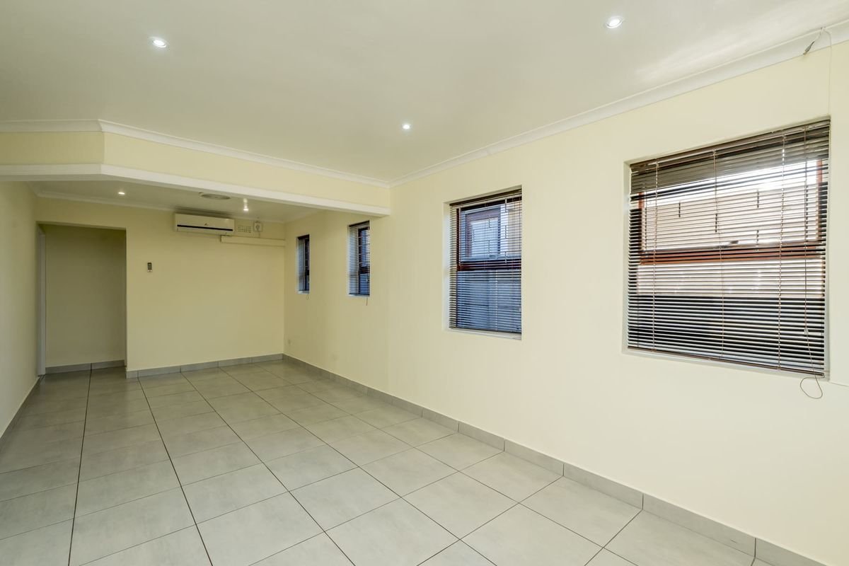 A bright, empty living area featuring neutral tiled flooring, recessed downlighting, and a wall-mounted air conditioning unit.