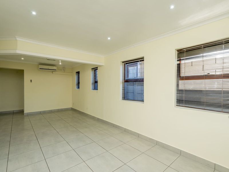 A bright, empty living area featuring neutral tiled flooring, recessed downlighting, and a wall-mounted air conditioning unit.