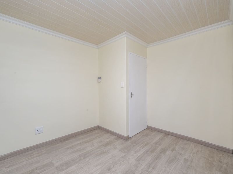A clean, empty bedroom featuring light-toned laminate flooring, built-in cupboards, and a coved ceiling, providing a neutral canvas for personalization.