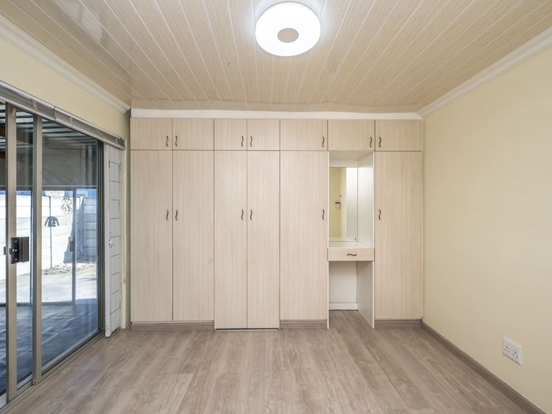 A bright, empty bedroom featuring extensive built-in cupboards with an integrated vanity, laminate flooring, and a sliding glass door leading to the exterior.