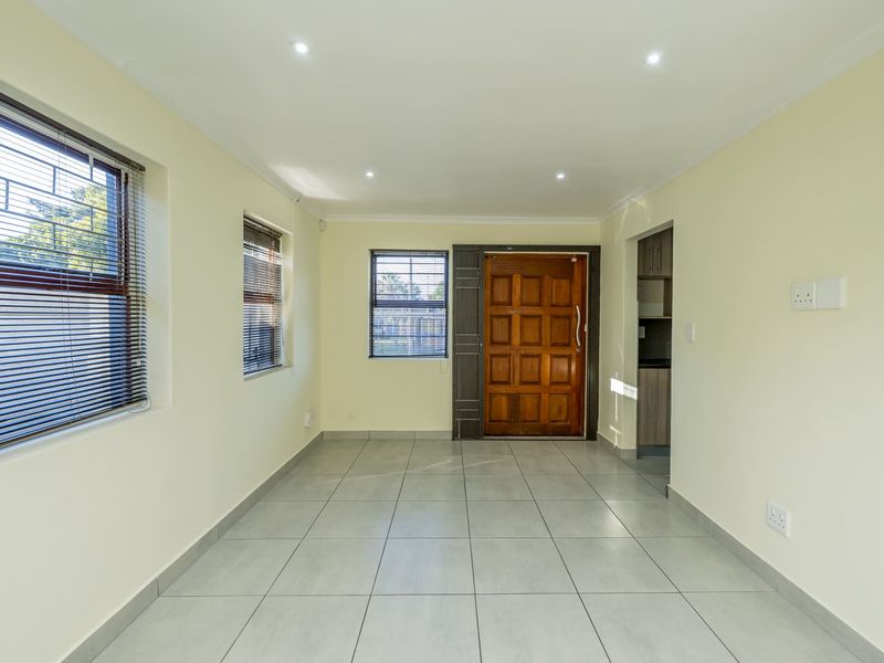 A bright, empty living area featuring neutral tiled flooring, recessed downlighting, and a solid timber front entrance door.