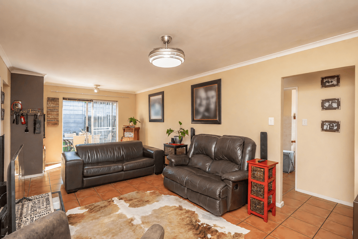 A comfortable living room featuring tiled flooring, a ceiling fan, and a sliding glass door providing access to the outdoor patio area.