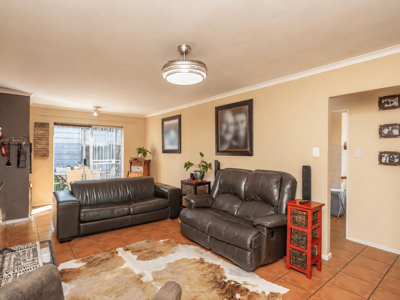 A comfortable living room featuring tiled flooring, a ceiling fan, and a sliding glass door providing access to the outdoor patio area.