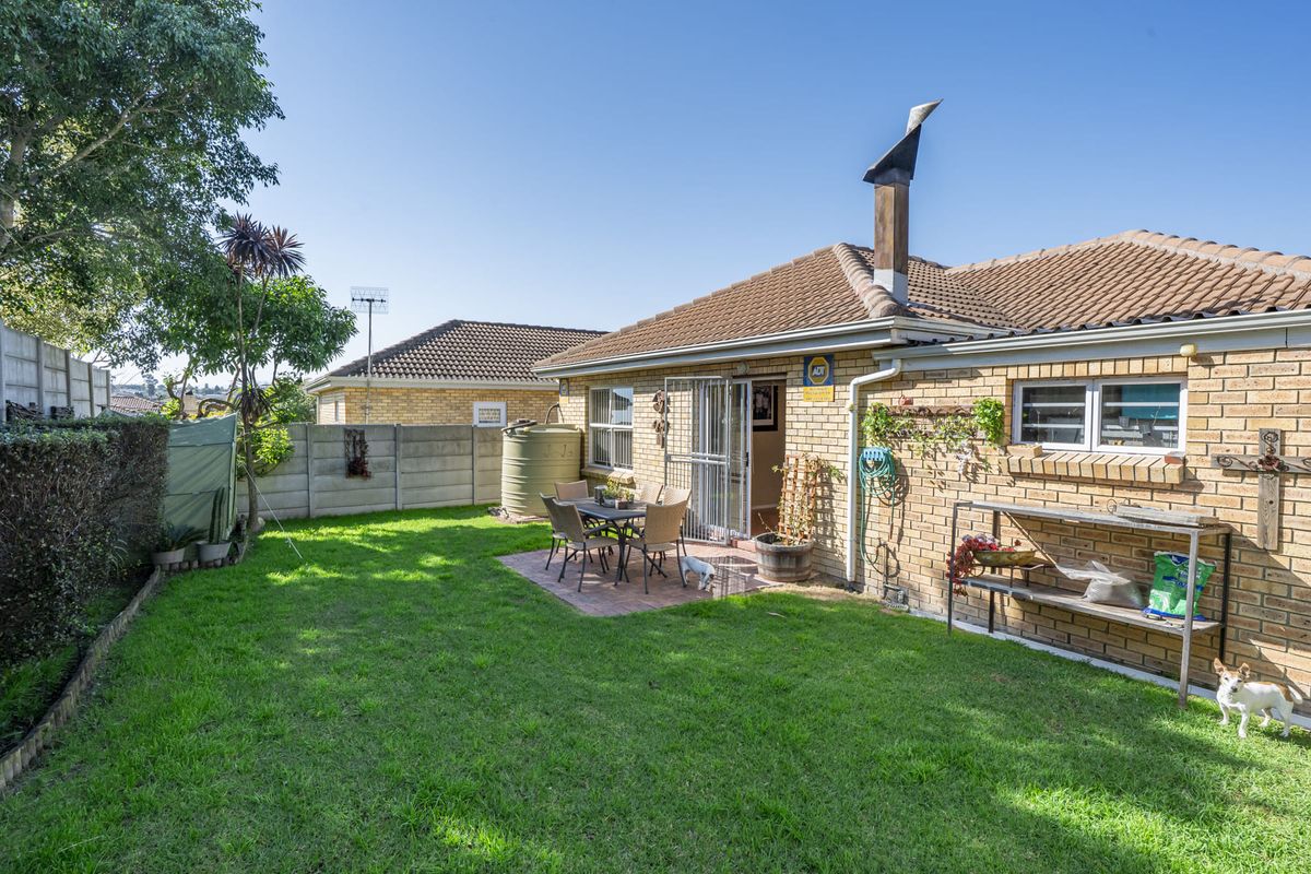 Rear view of the property featuring a brick facade, tiled roof, paved patio area, and a well-maintained garden with a water tank.