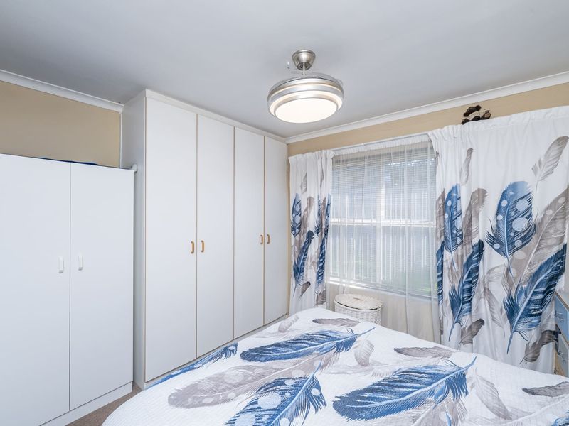 A bedroom featuring built-in cupboards, a ceiling fan, and window blinds, offering functional storage and lighting.