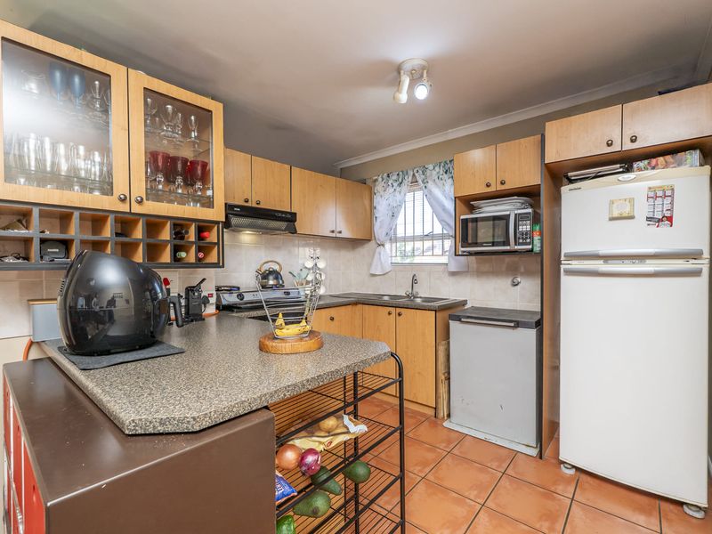 A functional kitchen featuring laminate cabinetry, tiled backsplash, and tiled flooring, offering a practical layout with built-in microwave and extractor fan.