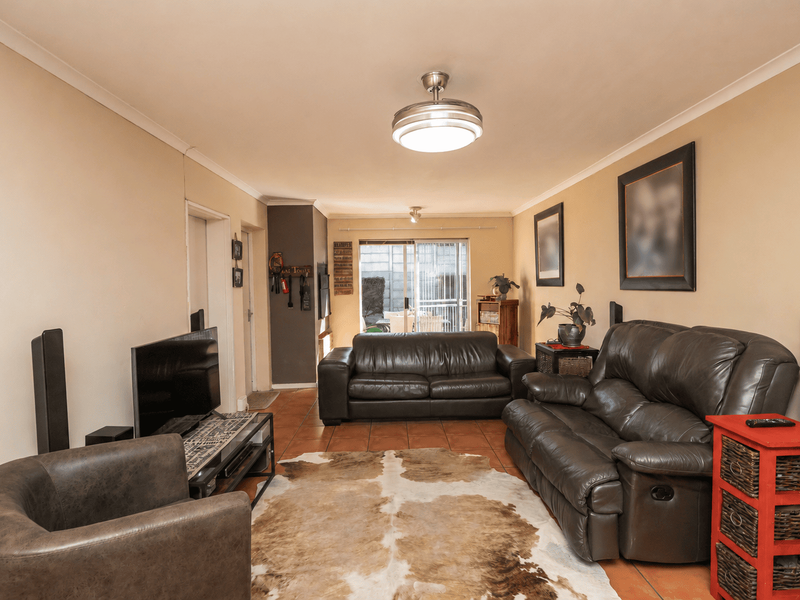 A comfortable living room featuring tiled flooring, a central ceiling fan, and sliding glass doors providing access to the outdoor area.