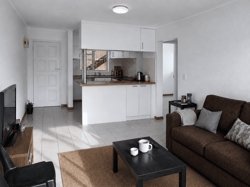 Open plan living area featuring a functional kitchen with white cabinetry, laminate countertops, and tiled flooring throughout the combined space.