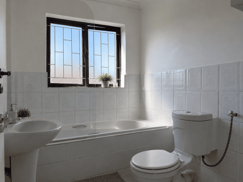 A functional bathroom featuring a pedestal basin, built-in bathtub with a glass screen, and a toilet, finished with white wall tiles.