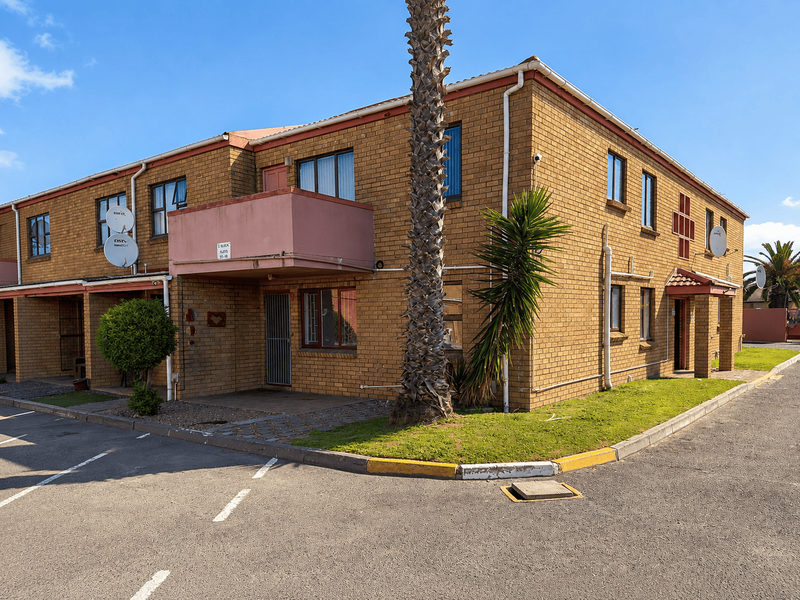 Exterior view of a face brick apartment building featuring a balcony, paved driveway, and established landscaping.
