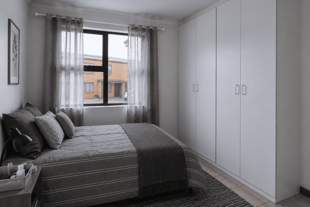 A well-maintained bedroom featuring neutral tiled flooring, built-in white cupboards, and an aluminium-framed window providing natural light.