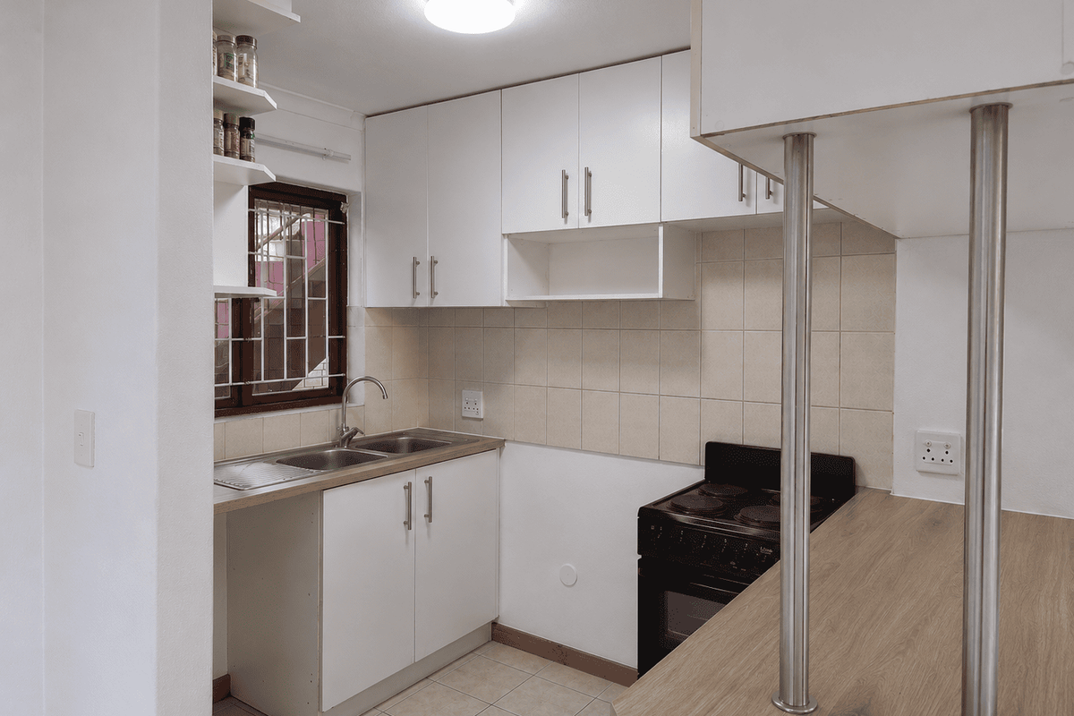A compact, functional kitchen featuring white cabinetry, a tiled backsplash, a breakfast bar with metal supports, and a freestanding stove.