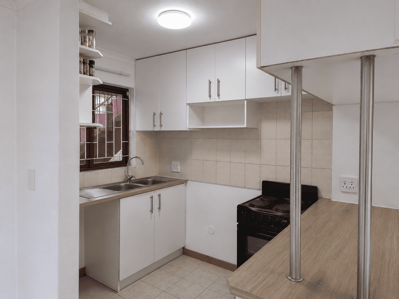 A compact, functional kitchen featuring white cabinetry, a tiled backsplash, a breakfast bar with metal supports, and a freestanding stove.