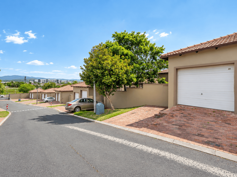 A street view of a townhouse complex featuring paved driveways, sectional garage doors, and well-maintained boundary walls under a clear blue sky.