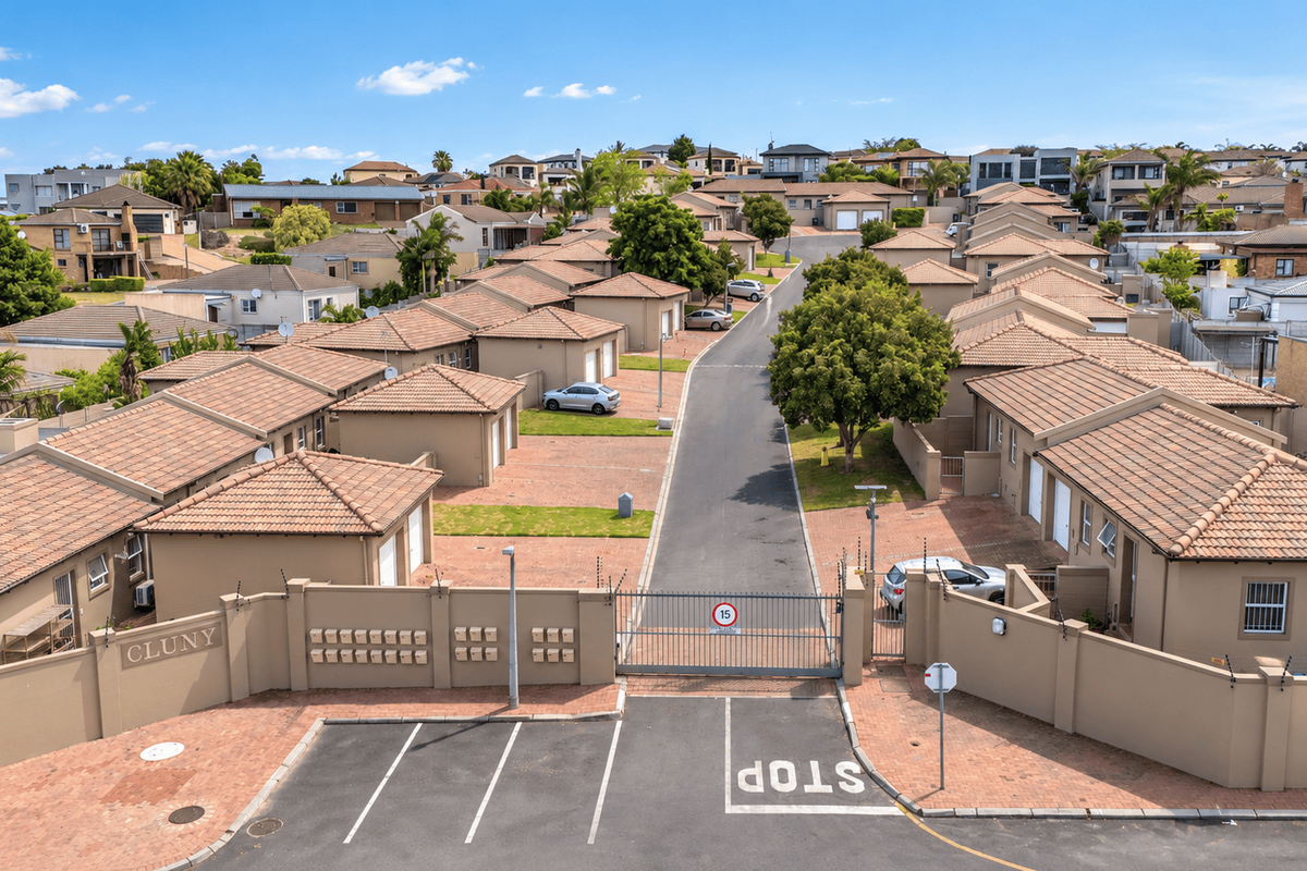 Aerial view of a secure residential townhouse complex featuring paved driveways, tiled roof units, and a gated entrance with perimeter security fencing.