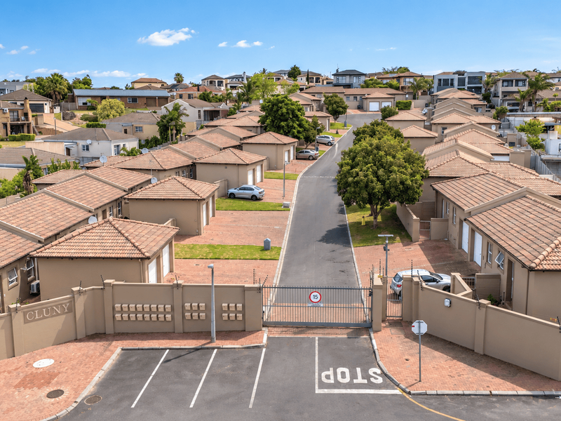 Aerial view of a secure residential townhouse complex featuring paved driveways, tiled roof units, and a gated entrance with perimeter security fencing.