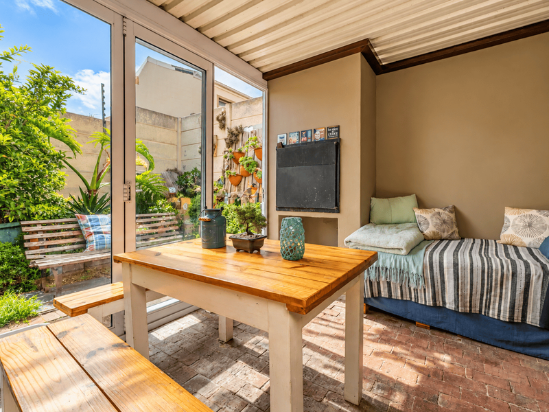 A covered patio area featuring brick flooring, a built-in wall niche, and large sliding glass doors that open to a private garden space.