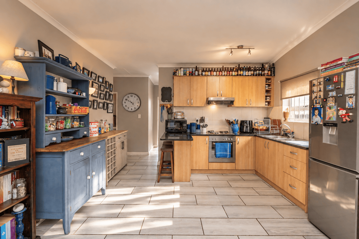 A functional kitchen featuring light wood cabinetry, integrated appliances, tiled flooring, and a dedicated prep area with additional storage cabinetry.