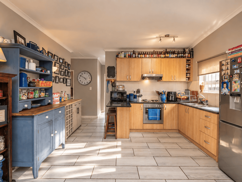 A functional kitchen featuring light wood cabinetry, integrated appliances, tiled flooring, and a dedicated prep area with additional storage cabinetry.