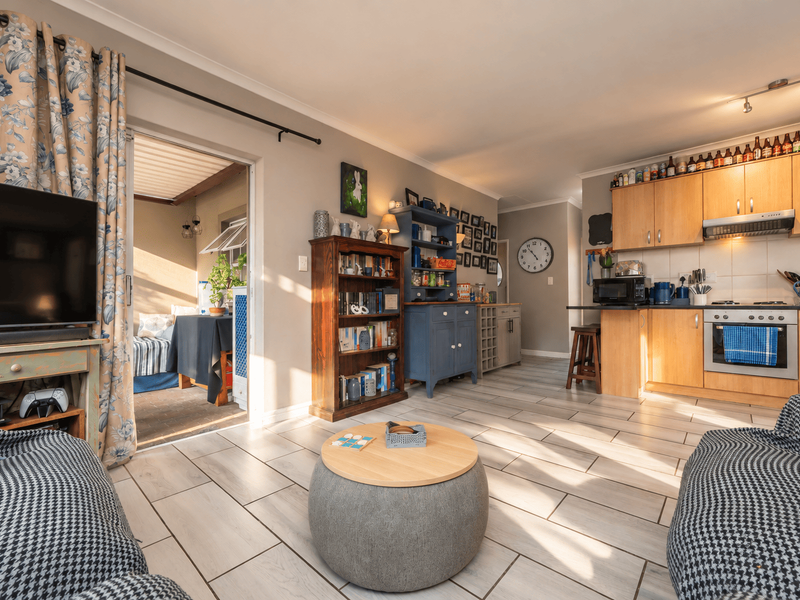 Open-plan living and kitchen area featuring light-toned tiled flooring, wooden cabinetry, and direct access to an outdoor patio space.