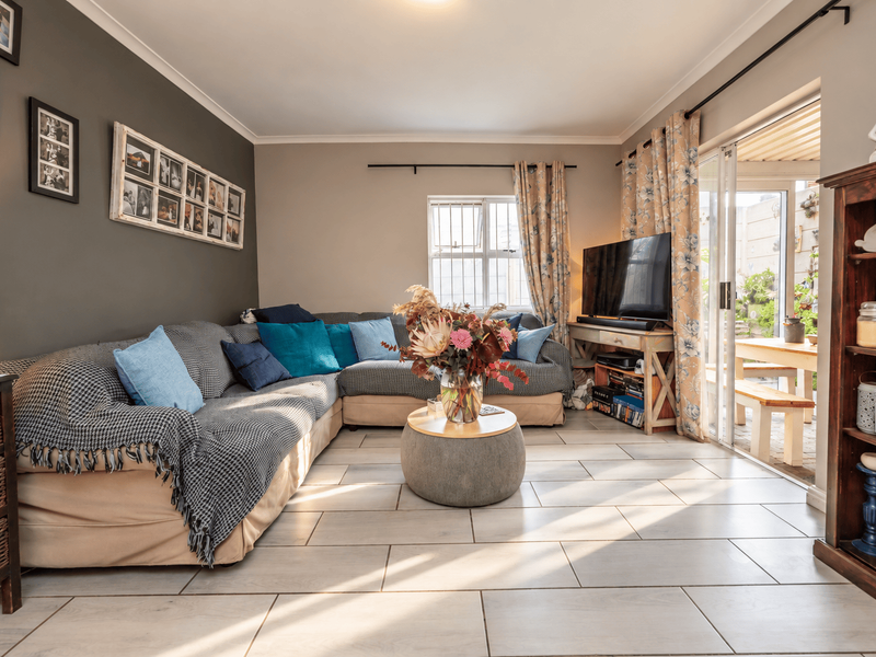 A well-lit living room featuring neutral tiled flooring, a feature wall, and large sliding glass doors providing direct access to an outdoor patio area.