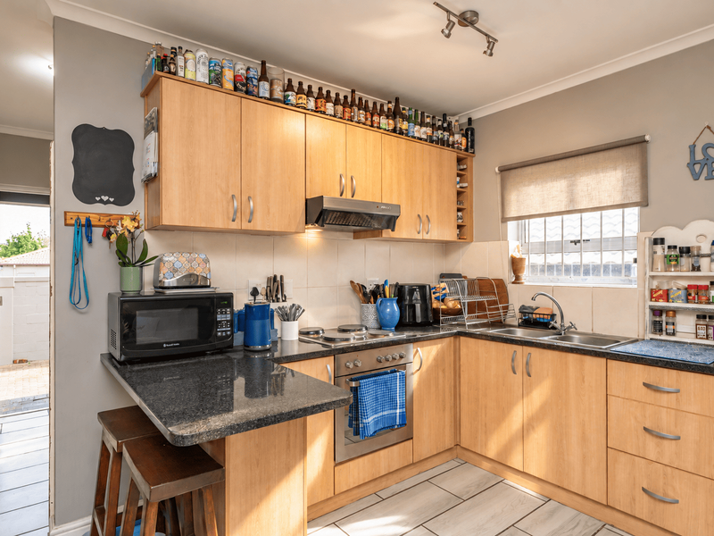 A functional kitchen featuring light wood cabinetry, granite countertops, built-in oven and hob, and tiled flooring with direct access to an outdoor area.