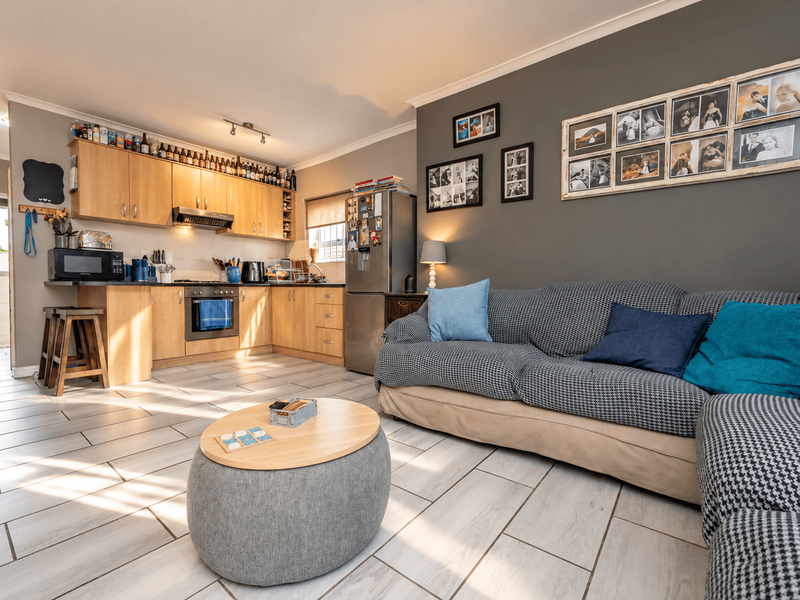 Open-plan living area featuring a functional kitchen with light wood cabinetry and tiled flooring, seamlessly connected to a comfortable lounge space.