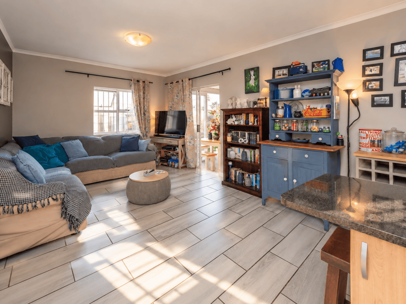 An open-plan living area featuring light-toned tiled flooring, a granite-topped breakfast bar, and a sliding door providing access to the patio.