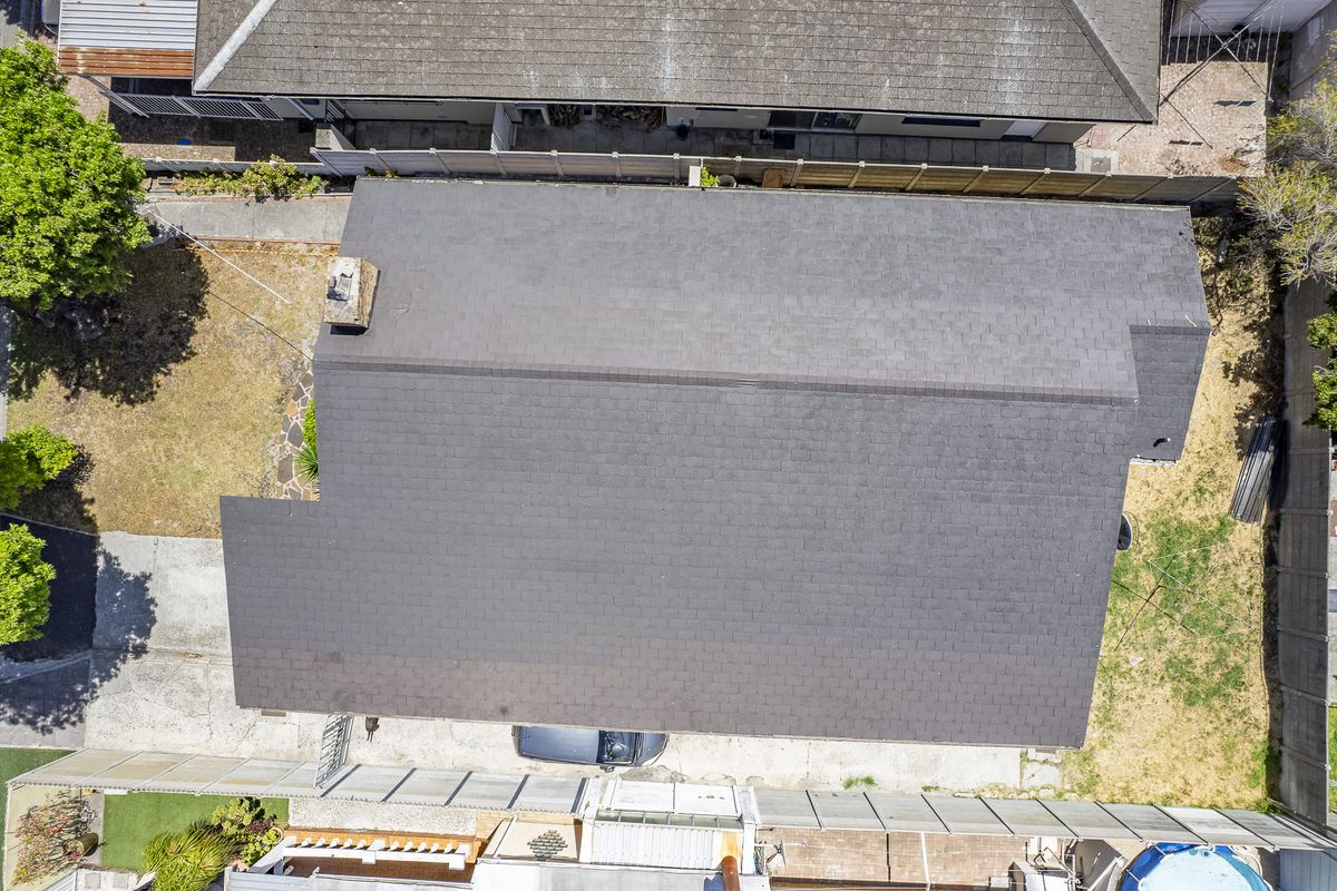 Aerial view of the property showing the main roof structure, brick chimney, surrounding yard space, and concrete driveway area.