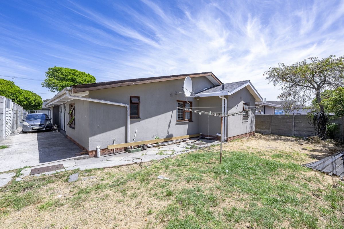 Rear view of the property featuring a concrete driveway, precast boundary wall, and a modest garden area with existing exterior infrastructure.