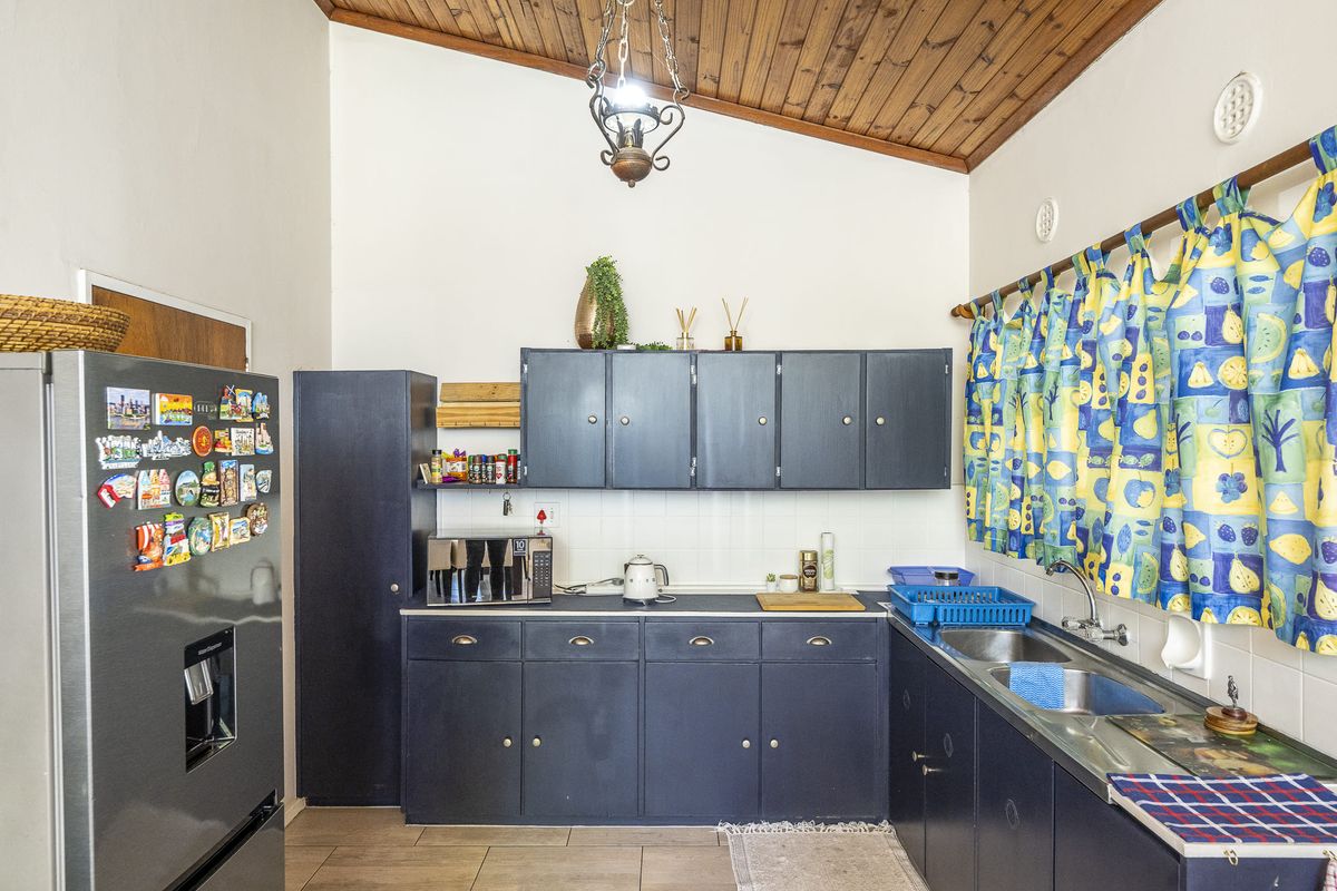 A functional kitchen featuring dark cabinetry, a double stainless steel sink, tiled backsplash, and a distinctive timber raked ceiling.