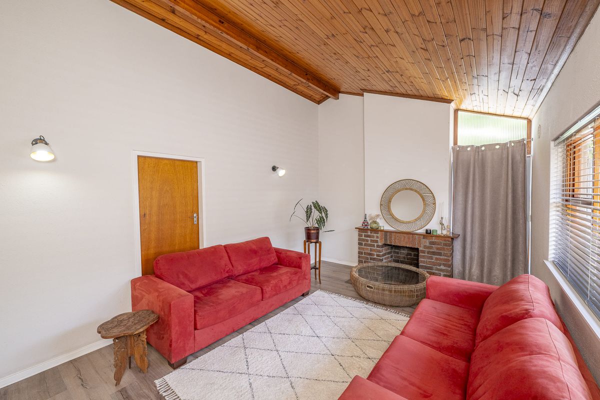 A living room featuring a high raked timber ceiling, brick fireplace, and modern laminate flooring, offering a cozy and character-filled space.