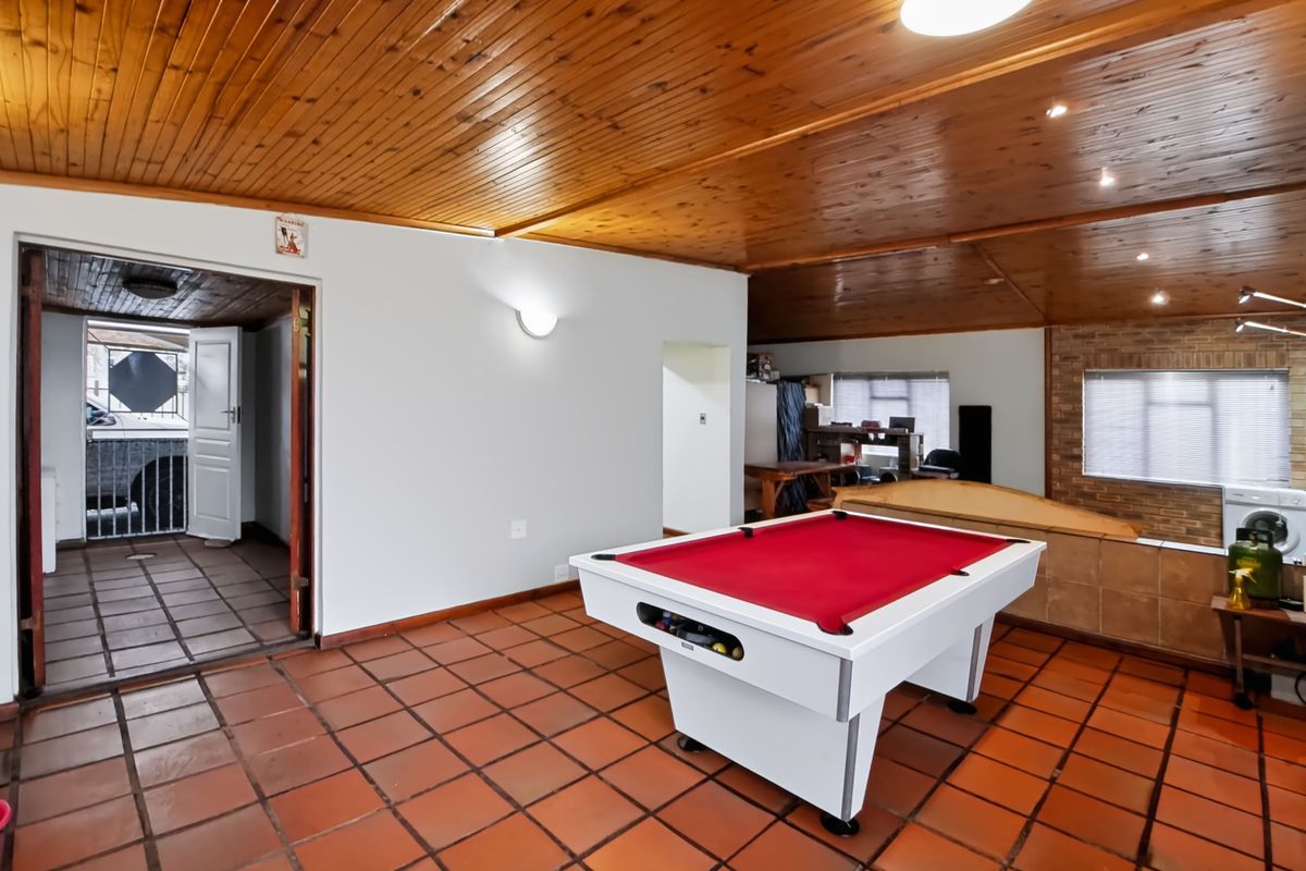 Spacious living area featuring terracotta floor tiles, a timber tongue and groove ceiling, and a brick feature wall, offering versatile space for recreation.