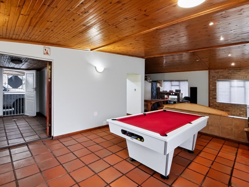Spacious living area featuring terracotta floor tiles, a timber tongue and groove ceiling, and a brick feature wall, offering versatile space for recreation.