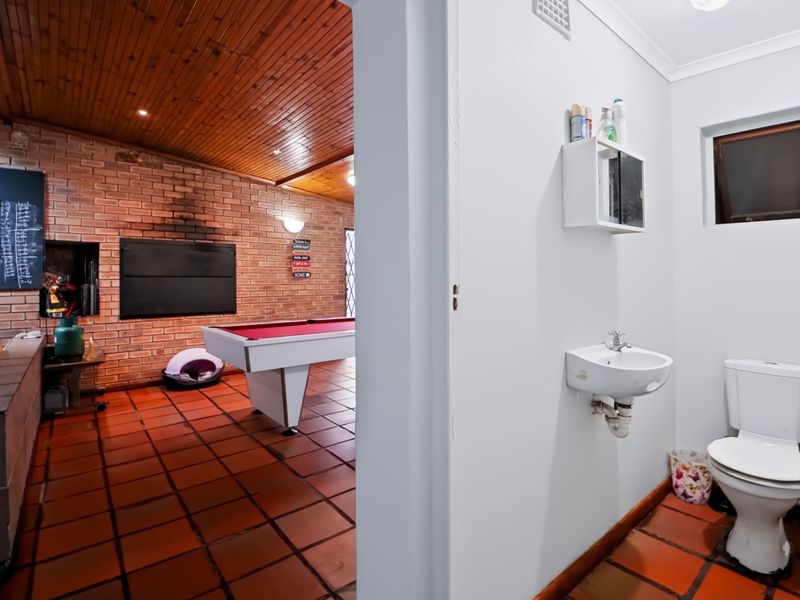 A view from a small bathroom into an adjacent entertainment room featuring exposed brick walls, a timber ceiling, and a built-in fireplace.