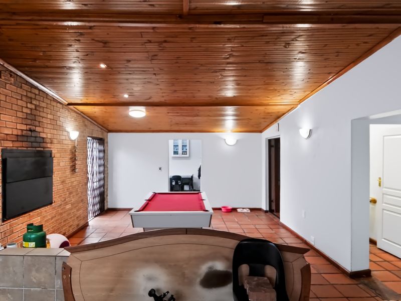 Spacious living area featuring a timber tongue and groove ceiling, exposed brick wall with a built-in fireplace, and terracotta floor tiles.
