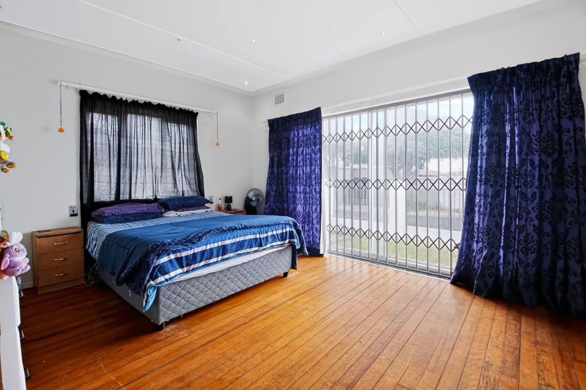 Spacious bedroom featuring original hardwood flooring, recessed lighting, and a large sliding glass door with a security gate leading to the exterior.