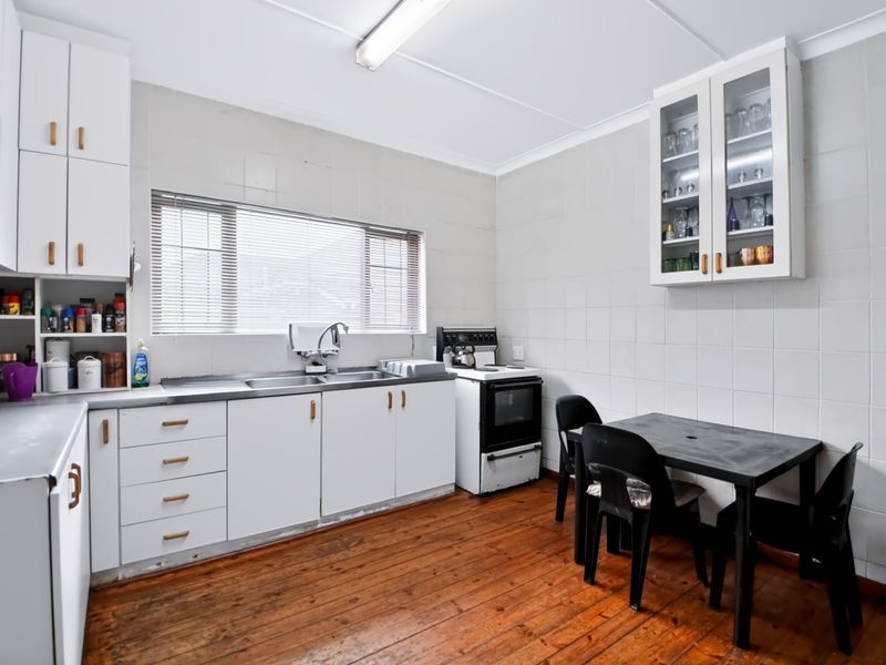 Functional kitchen featuring white cabinetry, tiled walls, stainless steel sink, and timber flooring, offering a practical layout with potential for modern updates.