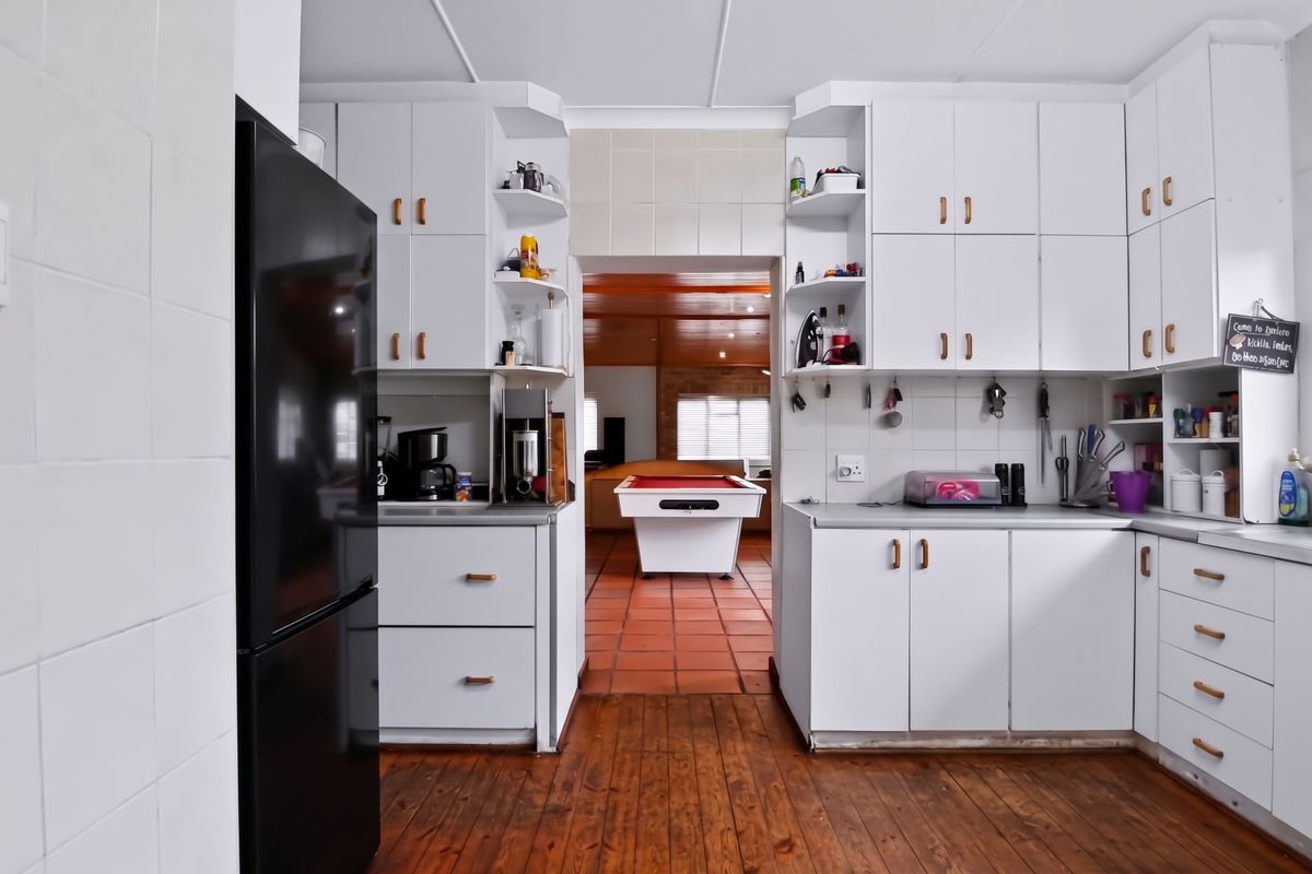 A functional kitchen featuring white built-in cabinetry, tiled backsplash, and wooden flooring, with a direct view into the adjacent living area.