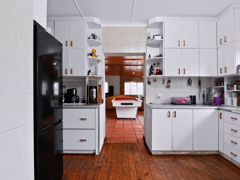 A functional kitchen featuring white built-in cabinetry, tiled backsplash, and wooden flooring, with a direct view into the adjacent living area.